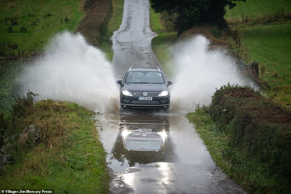 A car drives through a flooded road in the village of Bubnell in Derbyshire this morning as rain continues to fall in the region